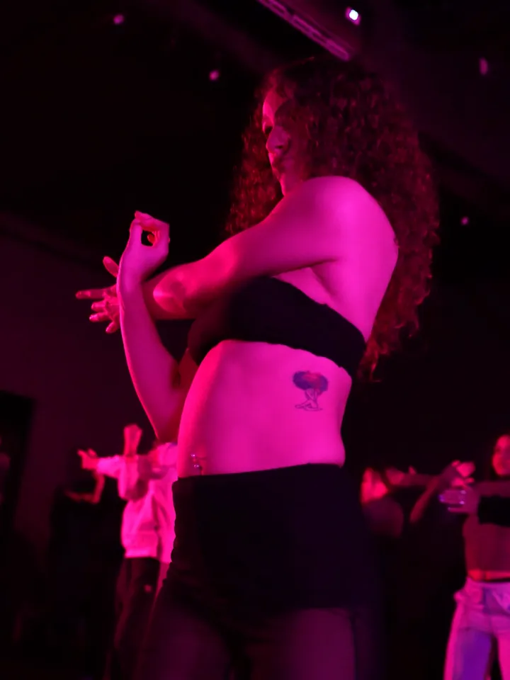 Bailarina en plena clase de heels dance, con el grupo detrás bajo luz rosa