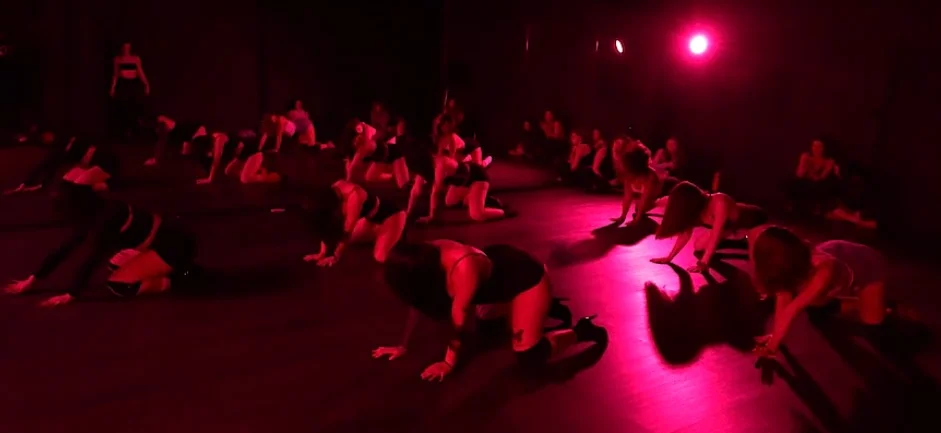 Una clase de On Heels llena: el grupo entero en el piso del estudio, en tacos, bajo un foco rosa